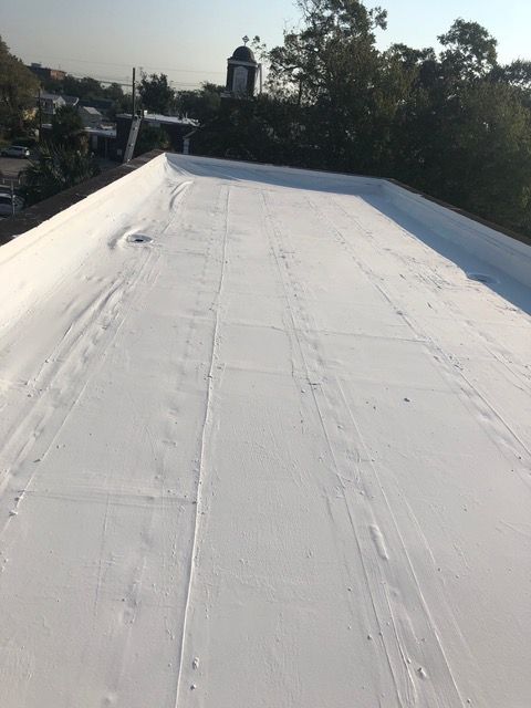 White flat roof with visible seams; trees and buildings in the background.