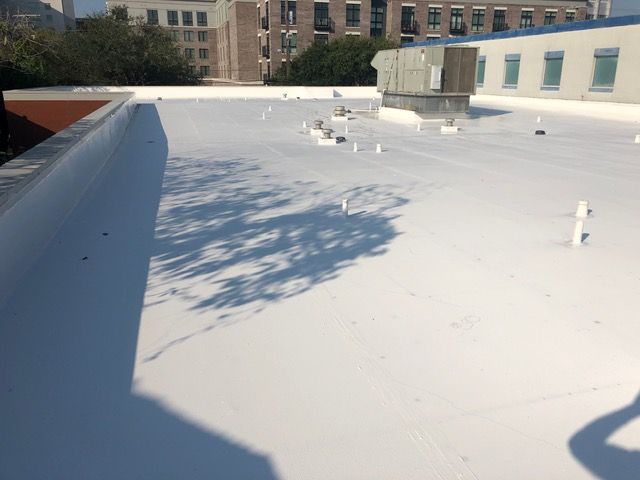 White flat roof with shadows, vents, and buildings in the background.