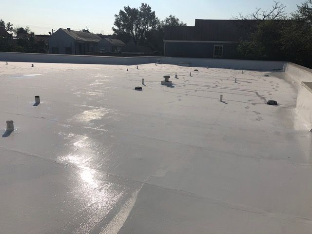 White flat roof on a building, reflecting sunlight. Several pipes and vents visible.