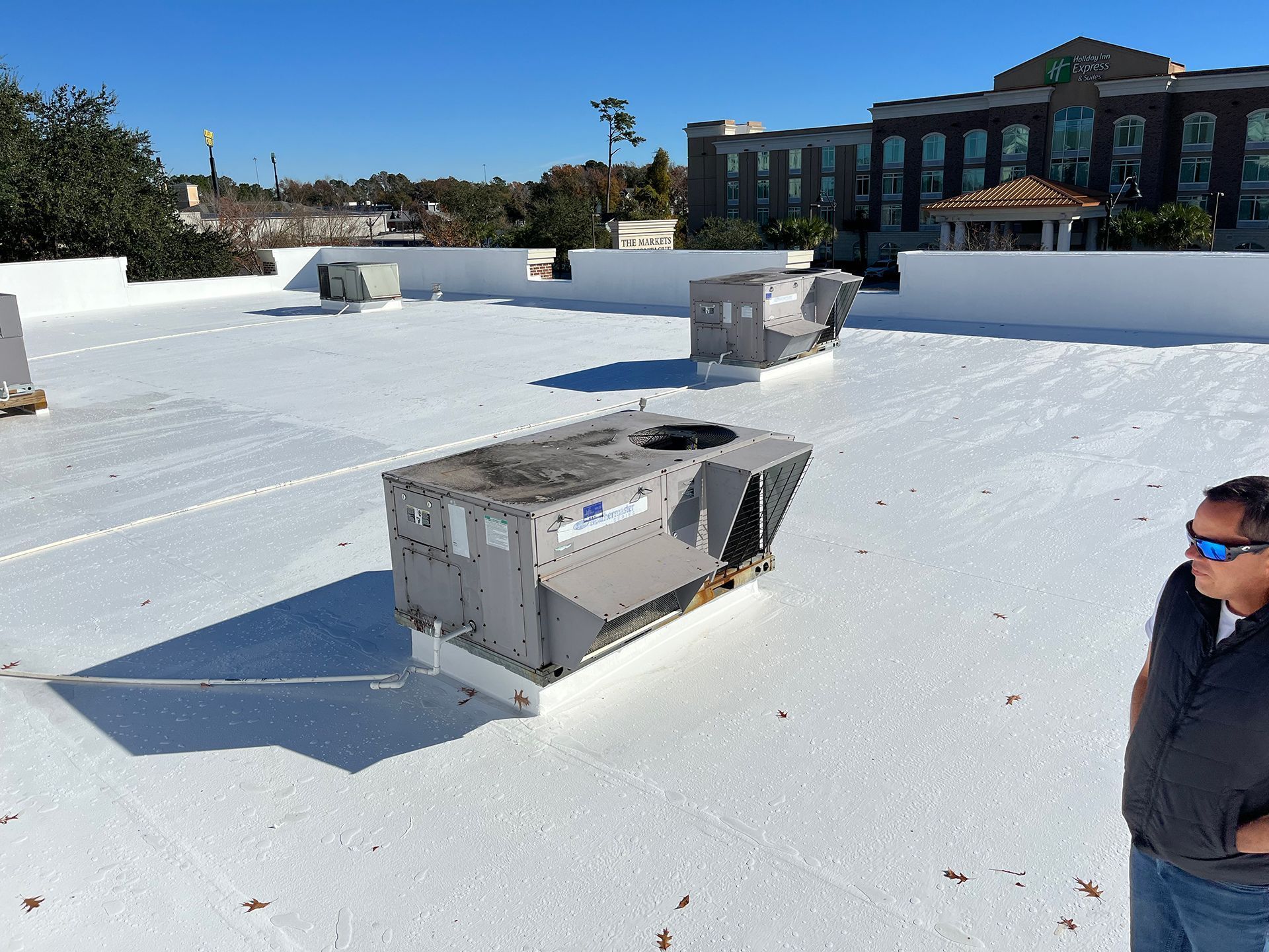 A person on a white commercial rooftop with HVAC units. Sunny day, modern building in background.