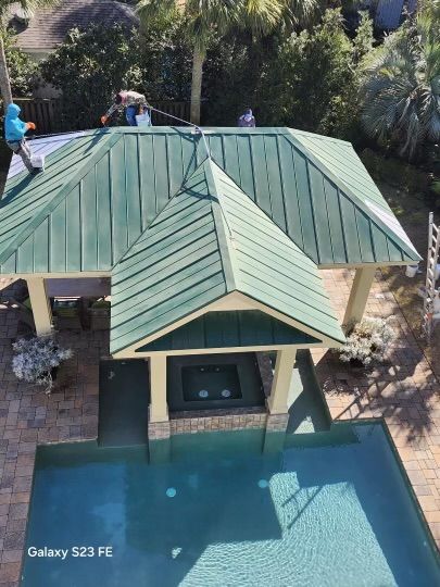Workers on a green metal roof of a gazebo over a pool.