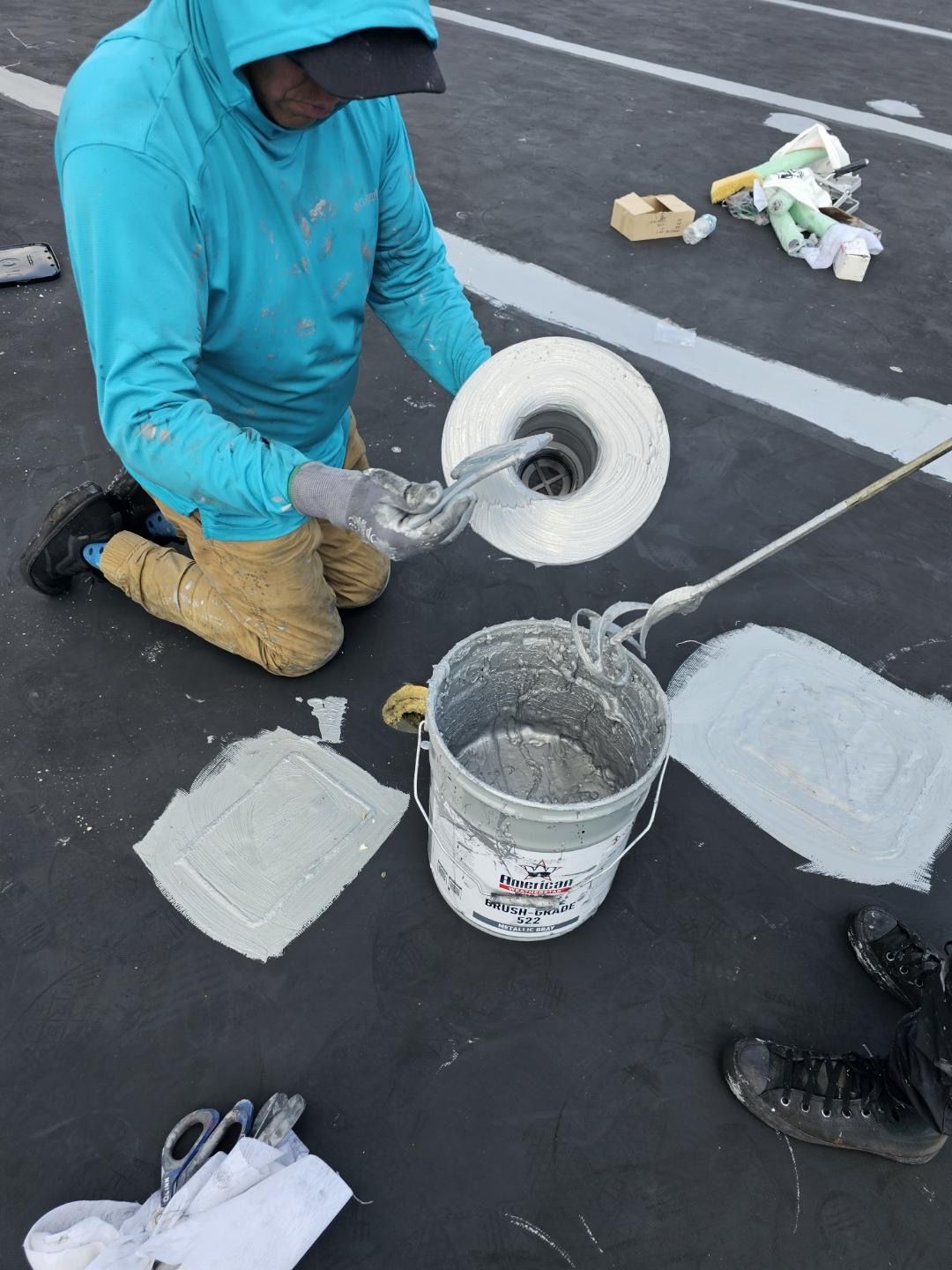 Person kneeling, handling a roll of white material and a bucket. They are on a dark surface, possibly a roof.