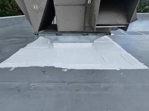 Gray flat roof with white sealant around a rectangular metal structure.