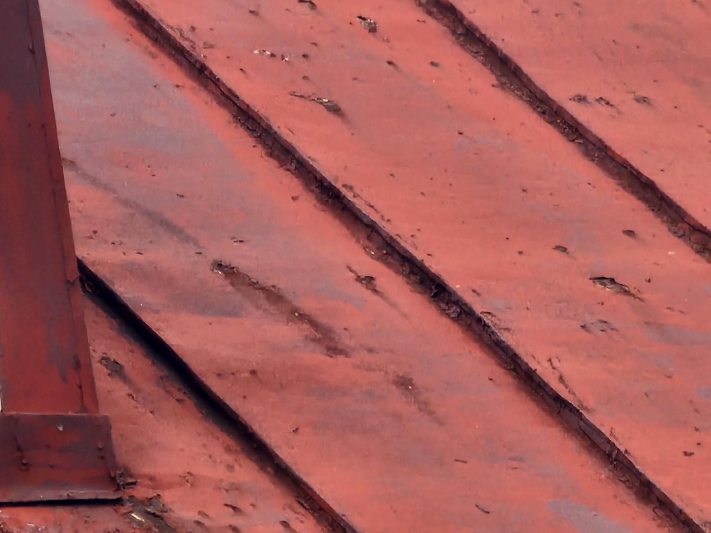 Red metal roof with ridged seams, showing wear and debris.