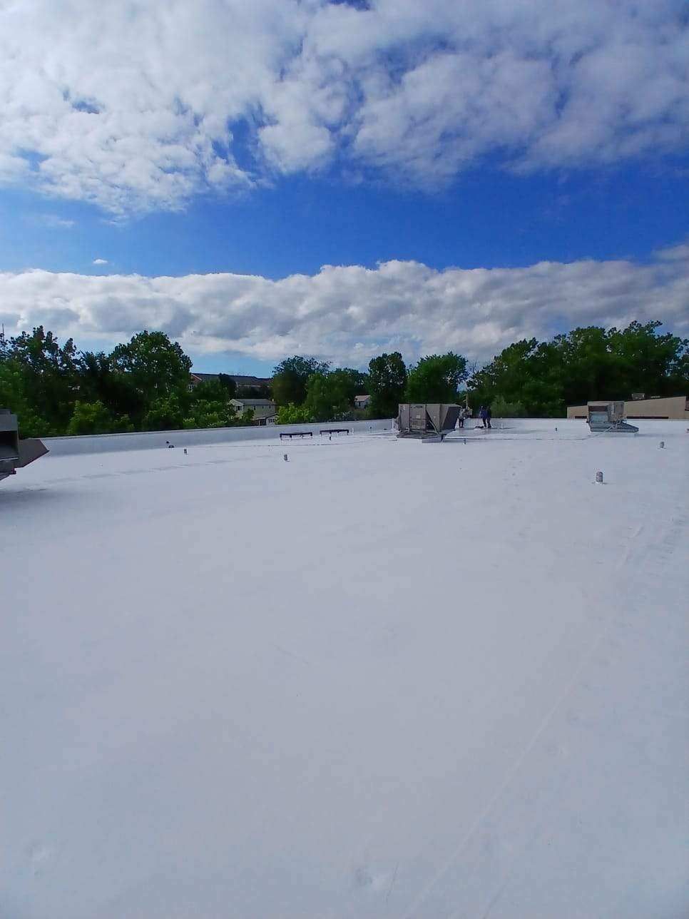 White rooftop with vents, trees in the background, blue sky with clouds.