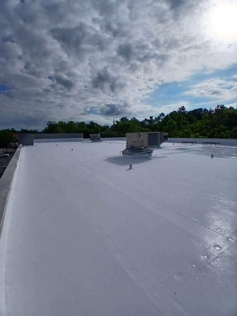 White coated commercial roof under a cloudy sky with rooftop vents visible.