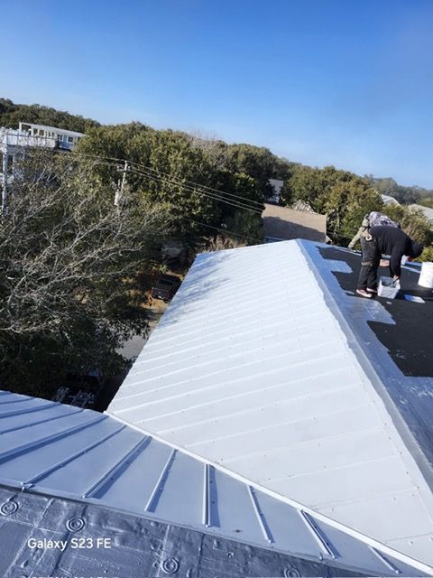 Person painting a light gray metal roof on a sunny day.