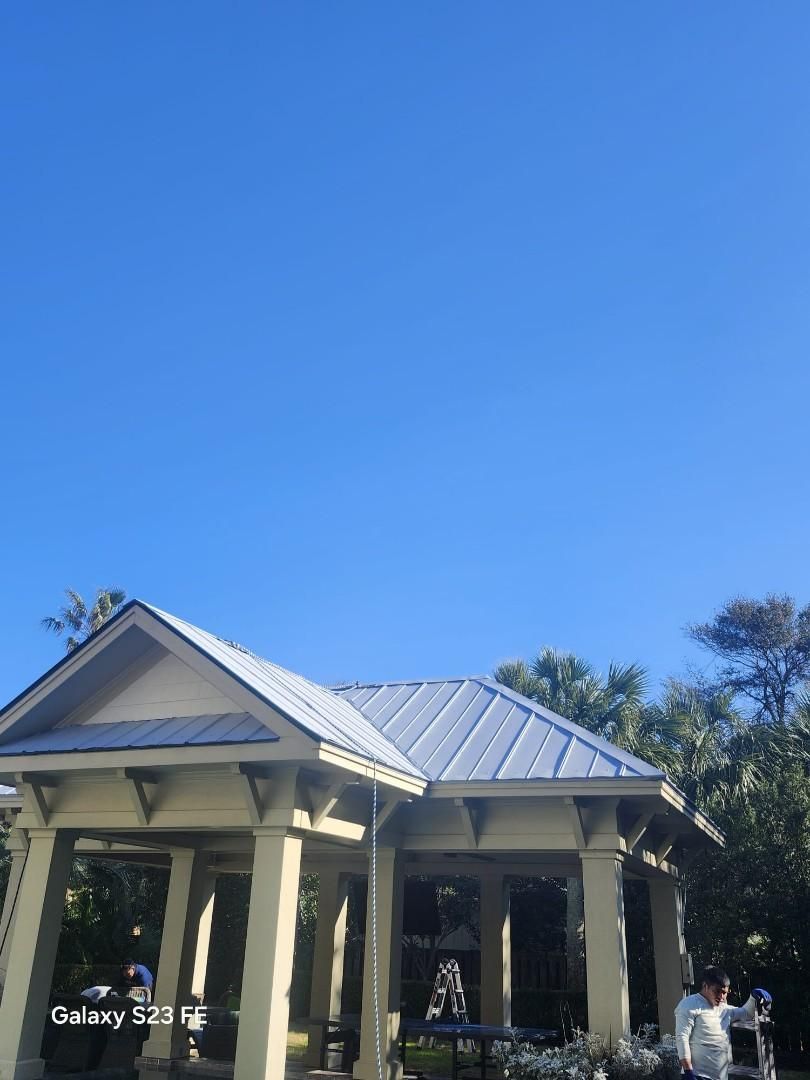 Pavilion with silver roof and light-colored supports against a bright blue sky.