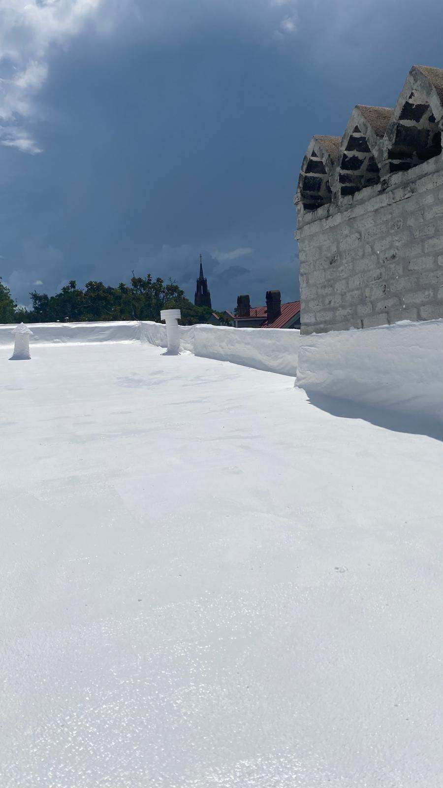 White rooftop with a cloudy sky backdrop. Buildings and a church steeple are visible in the distance.