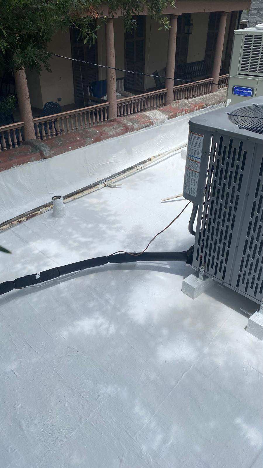 A white flat roof with an air conditioning unit and black electrical conduit.