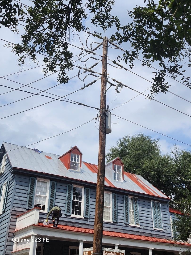 Wooden utility pole with transformer, wires, and a historic blue house with a red roof.