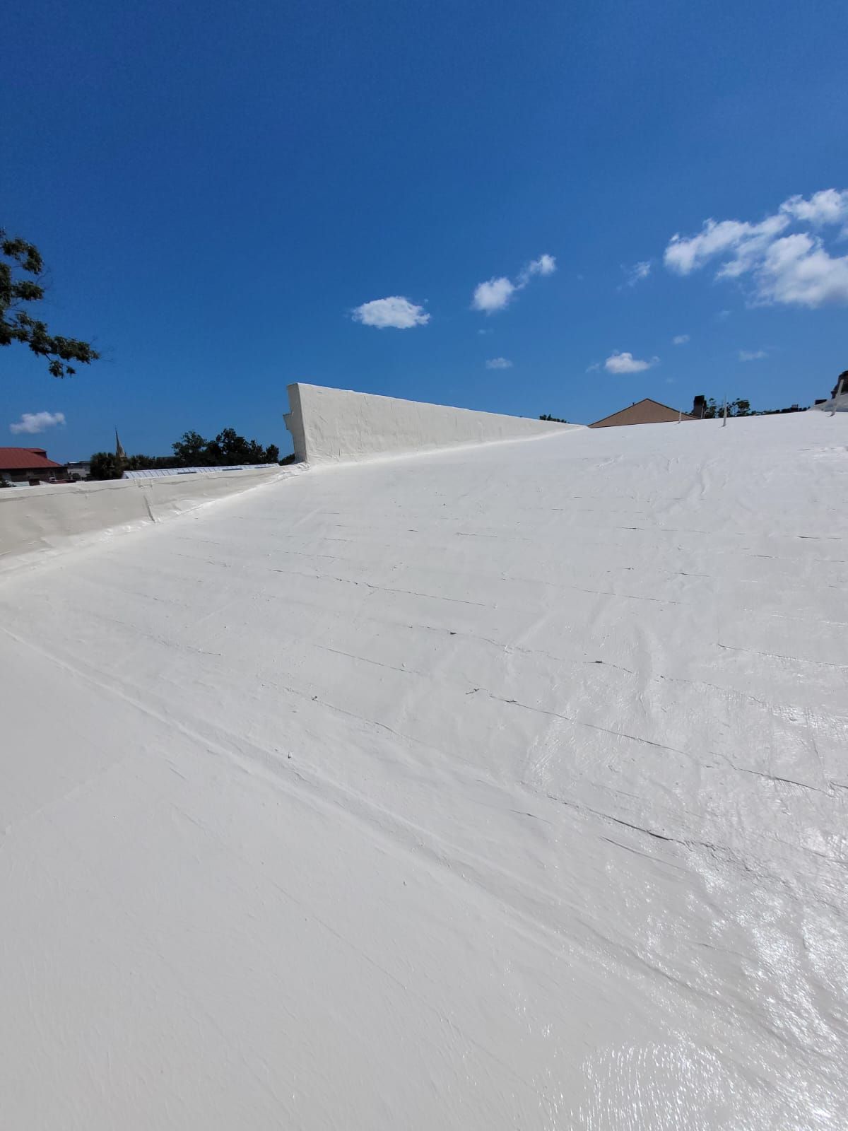 White roof coated with sealant against a clear blue sky with some clouds.