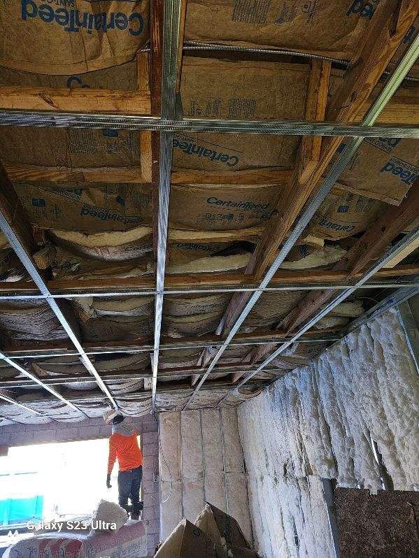 Interior ceiling view during renovation; exposed wood, metal supports, insulation; person in the background.