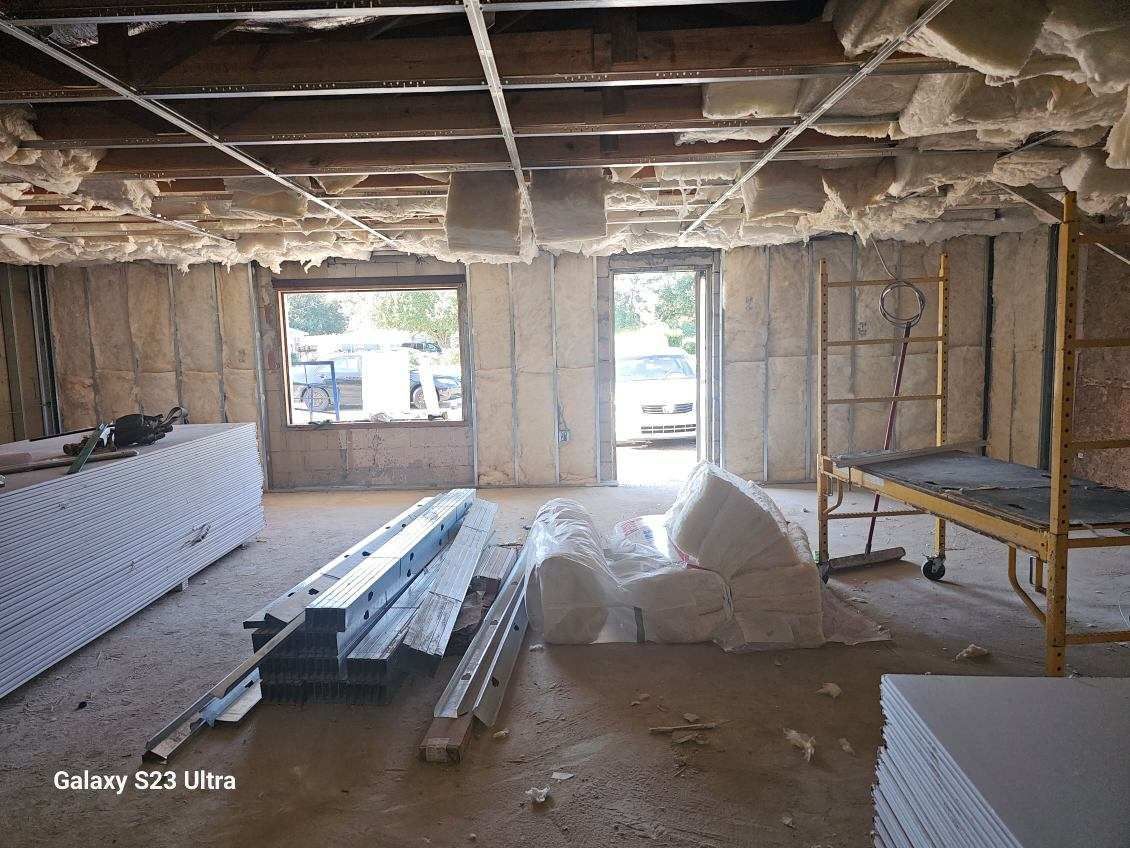 Interior of a room under construction with exposed insulation, framing, and drywall materials.