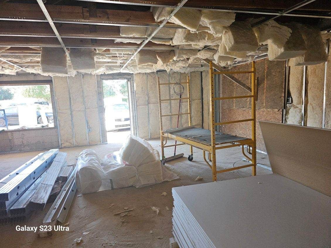Interior construction site with insulation in walls and ceiling, scaffolding, and drywall sheets.