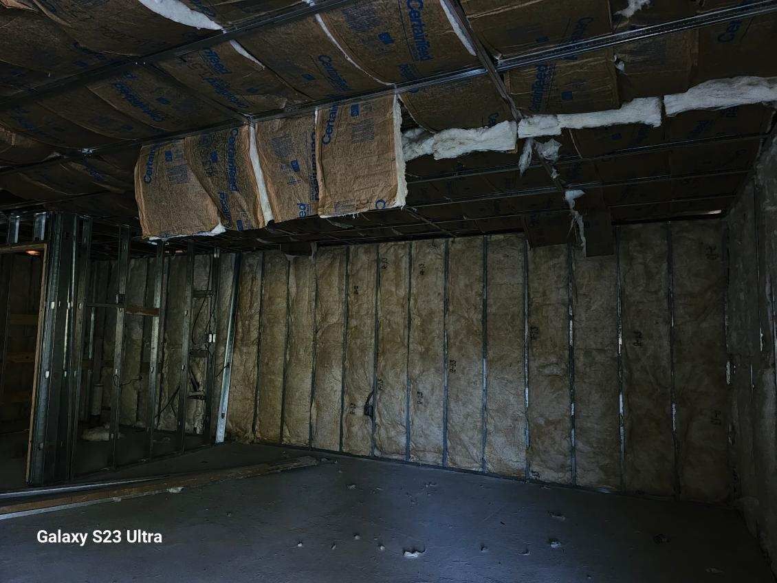 Interior view of unfinished construction. Insulation on walls and ceiling, metal framing, dark concrete floor.