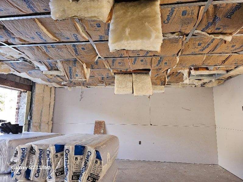 Interior view of a room under construction with exposed insulation, drywall, and stacks of packaged insulation.
