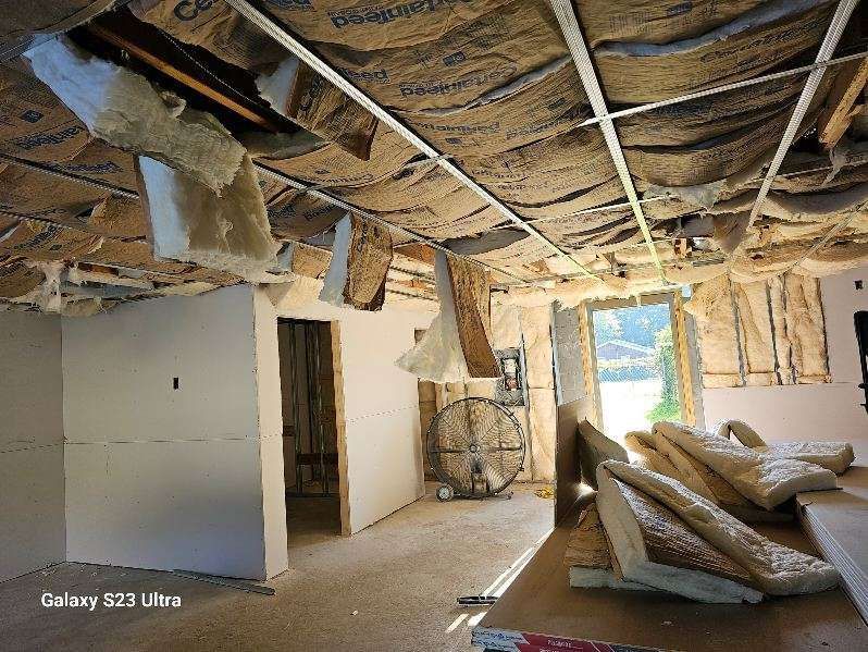 Interior of a building under renovation, exposed ceiling insulation and framing. Sunlight streams in from a doorway.