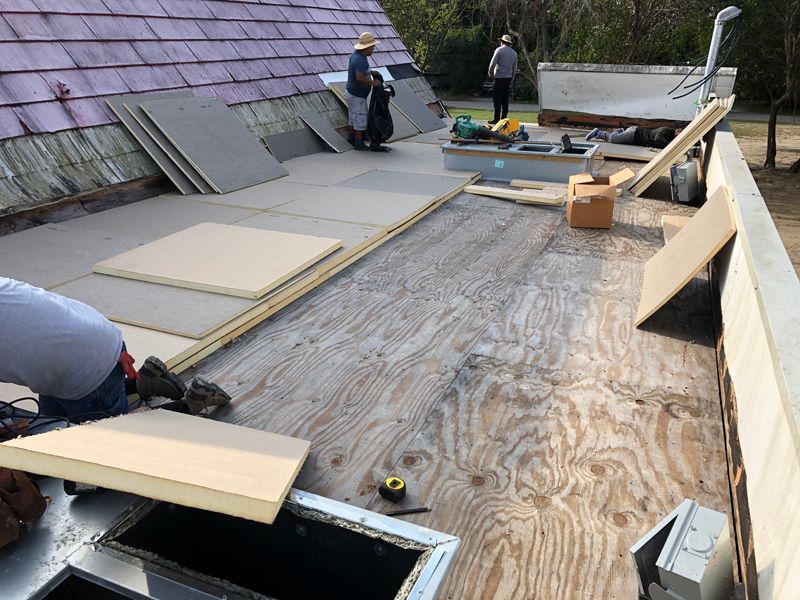 Workers renovating a roof, laying plywood and insulation. Tools and materials are scattered.