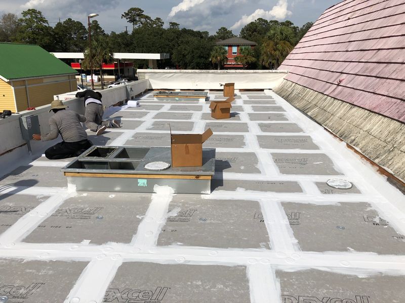 Workers sealing a flat roof with white sealant; boxes and tools visible.
