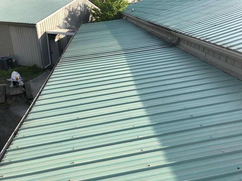 Green metal roof on a building, with visible ridges, reflecting sunlight.