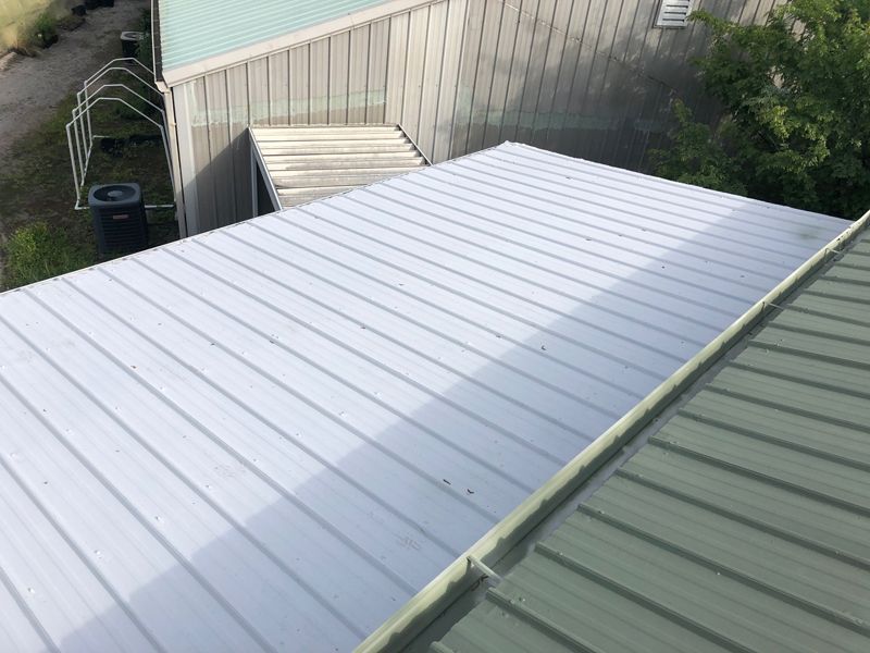 Overhead view of two metal roofs, one silver and one green, with a building in the background.