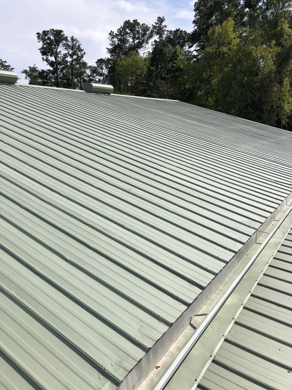 Green metal roof with ribbed panels, angled upward toward trees and sky.