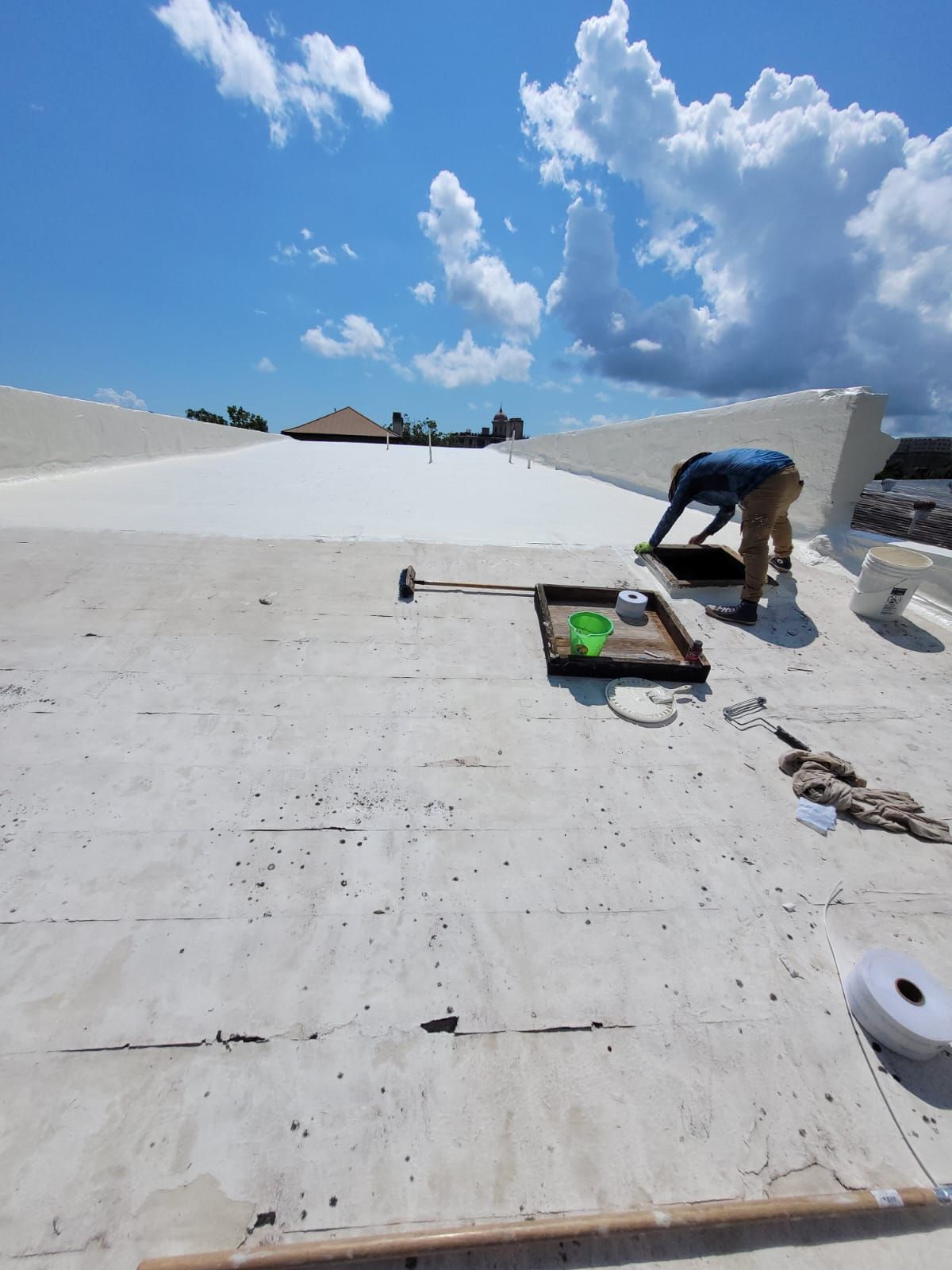 Two workers applying roofing material with a torch and roller on a dark surface.