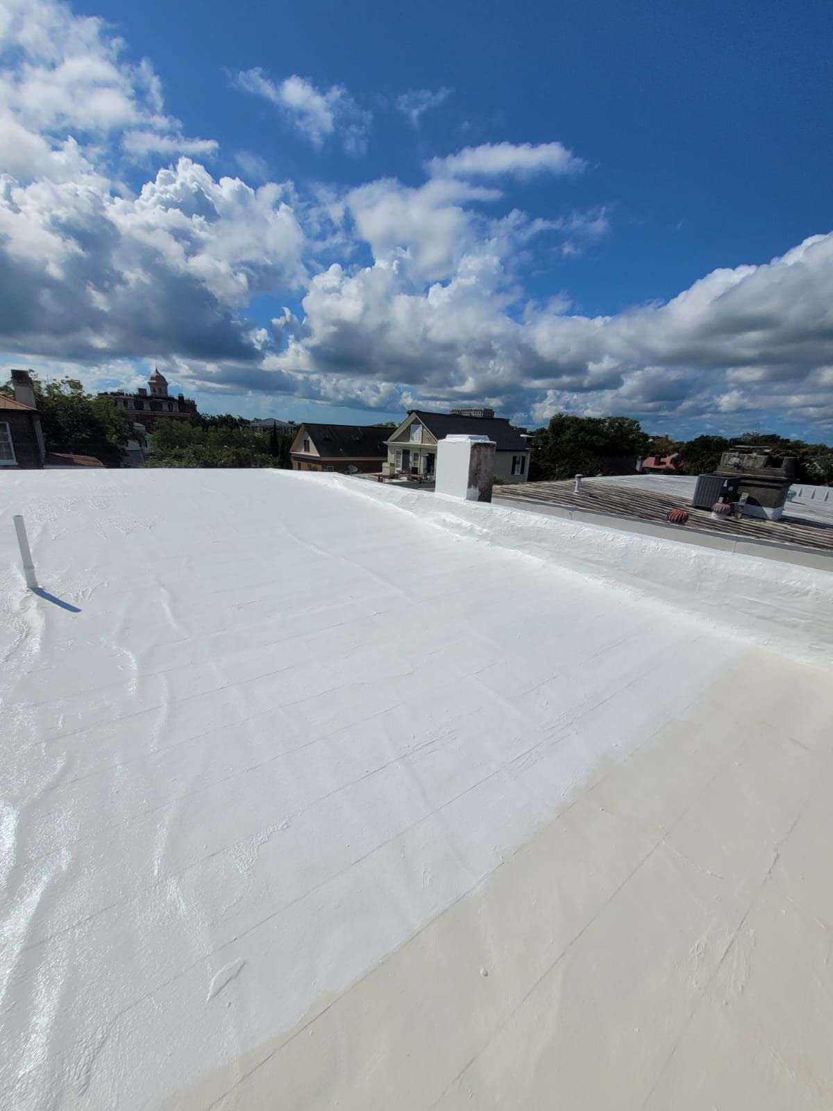 White roof with buildings in the background under a blue sky with clouds.