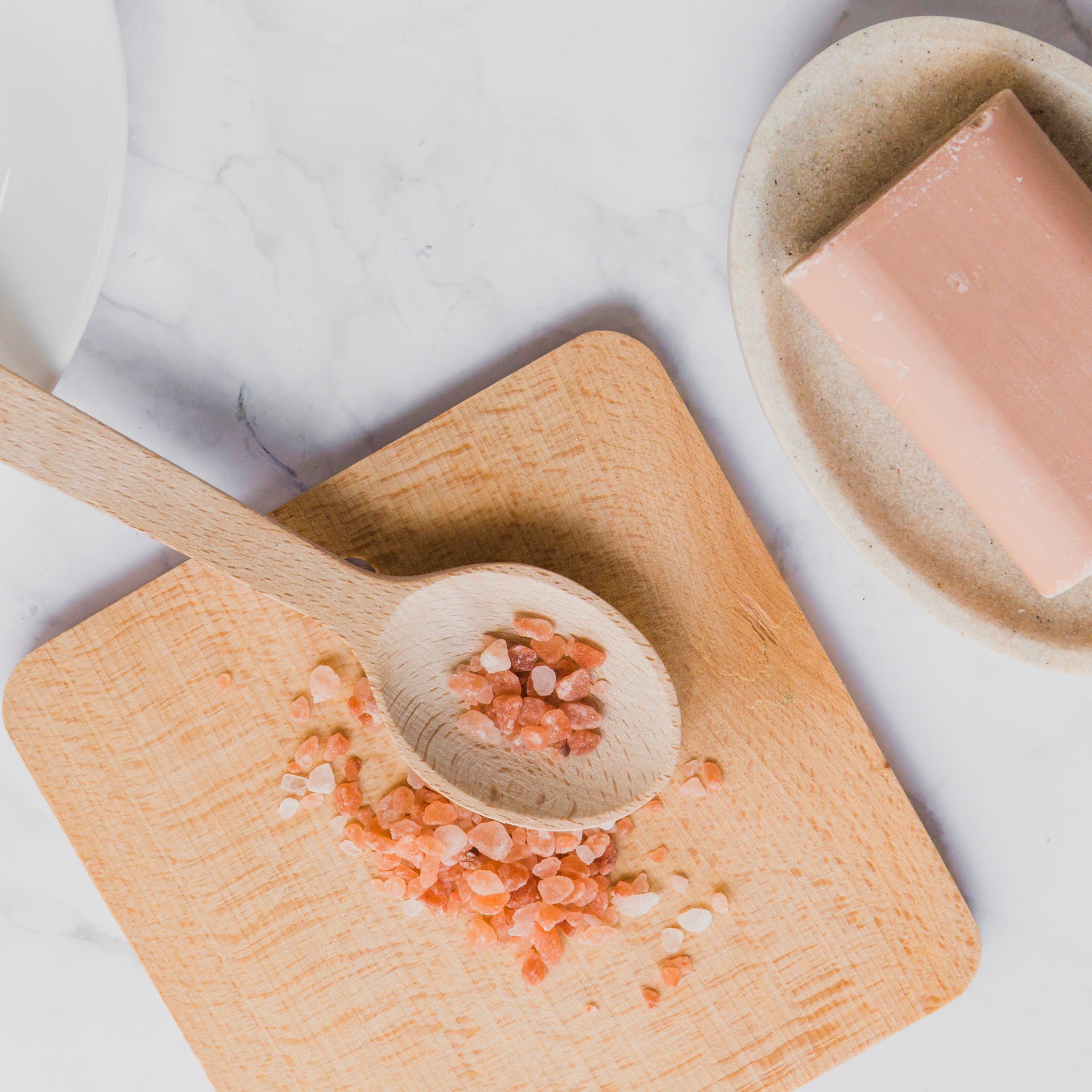 Un cucchiaio di legno pieno di sale rosa è appoggiato su un tagliere di legno