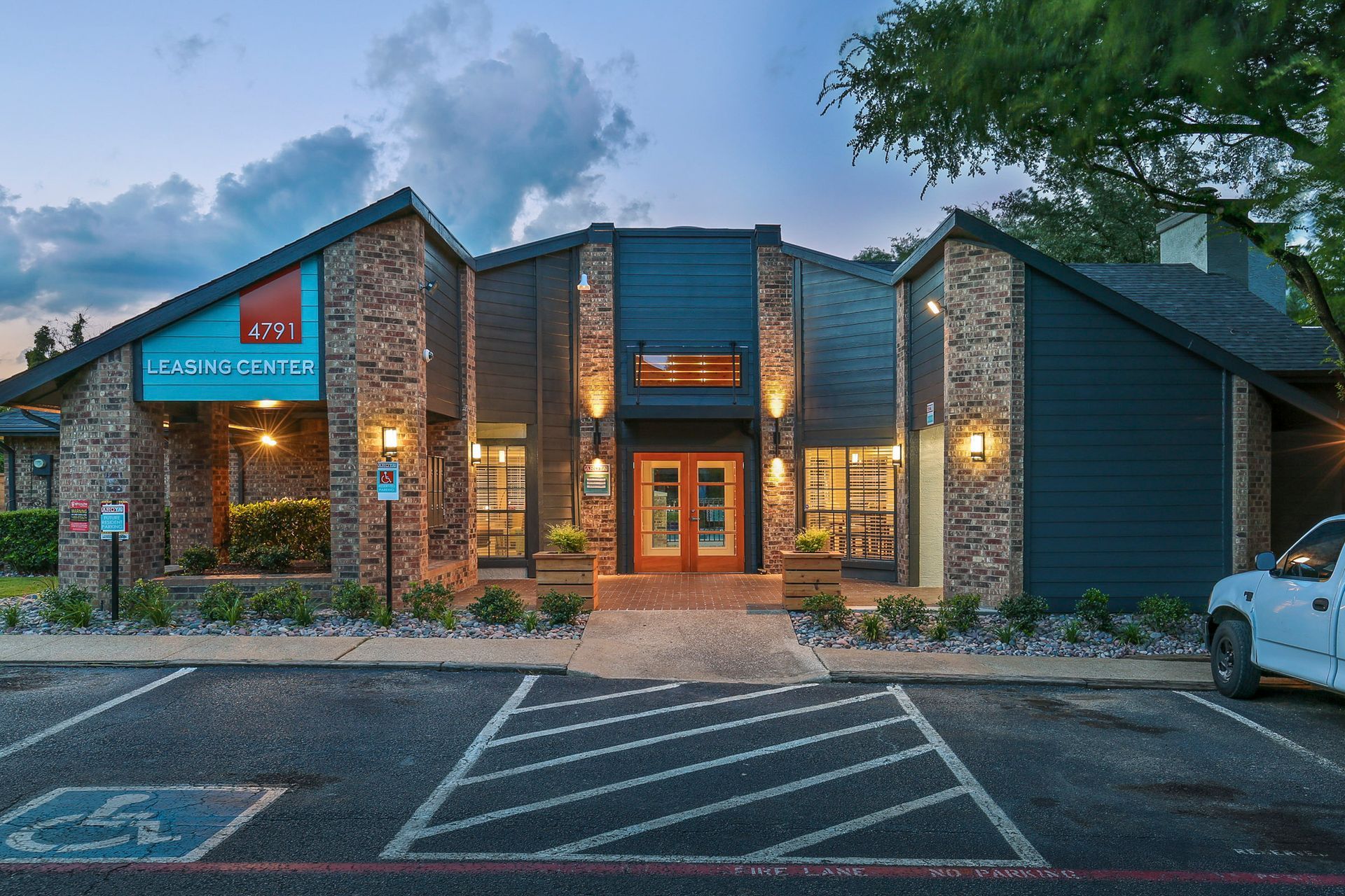 Exterior view of a leasing office with a brick facade and blue siding; a white truck is parked nearby.