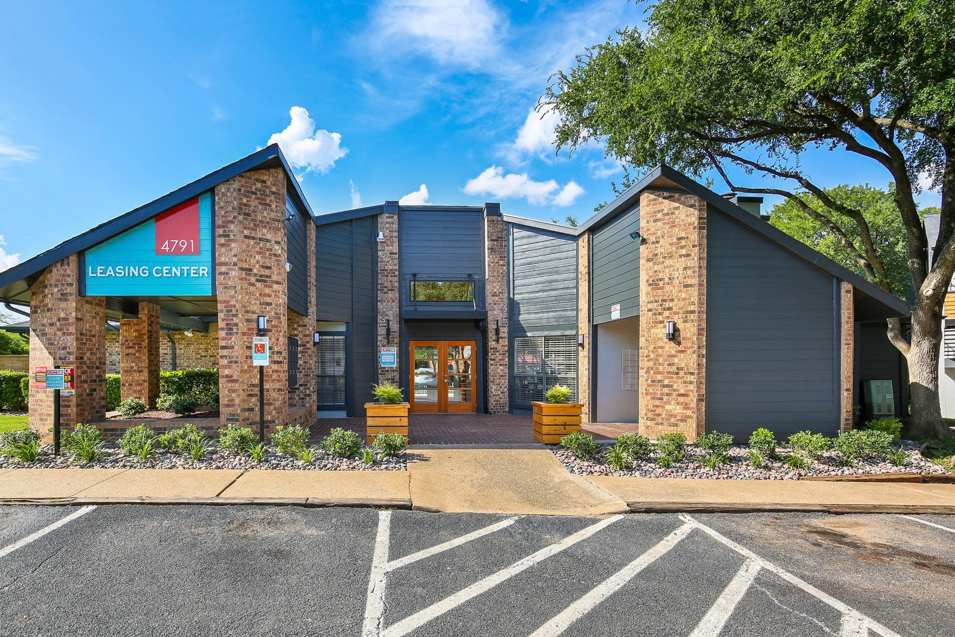 Apartment leasing center with brick and gray exterior, blue accents, and entrance. Bright sunny day.