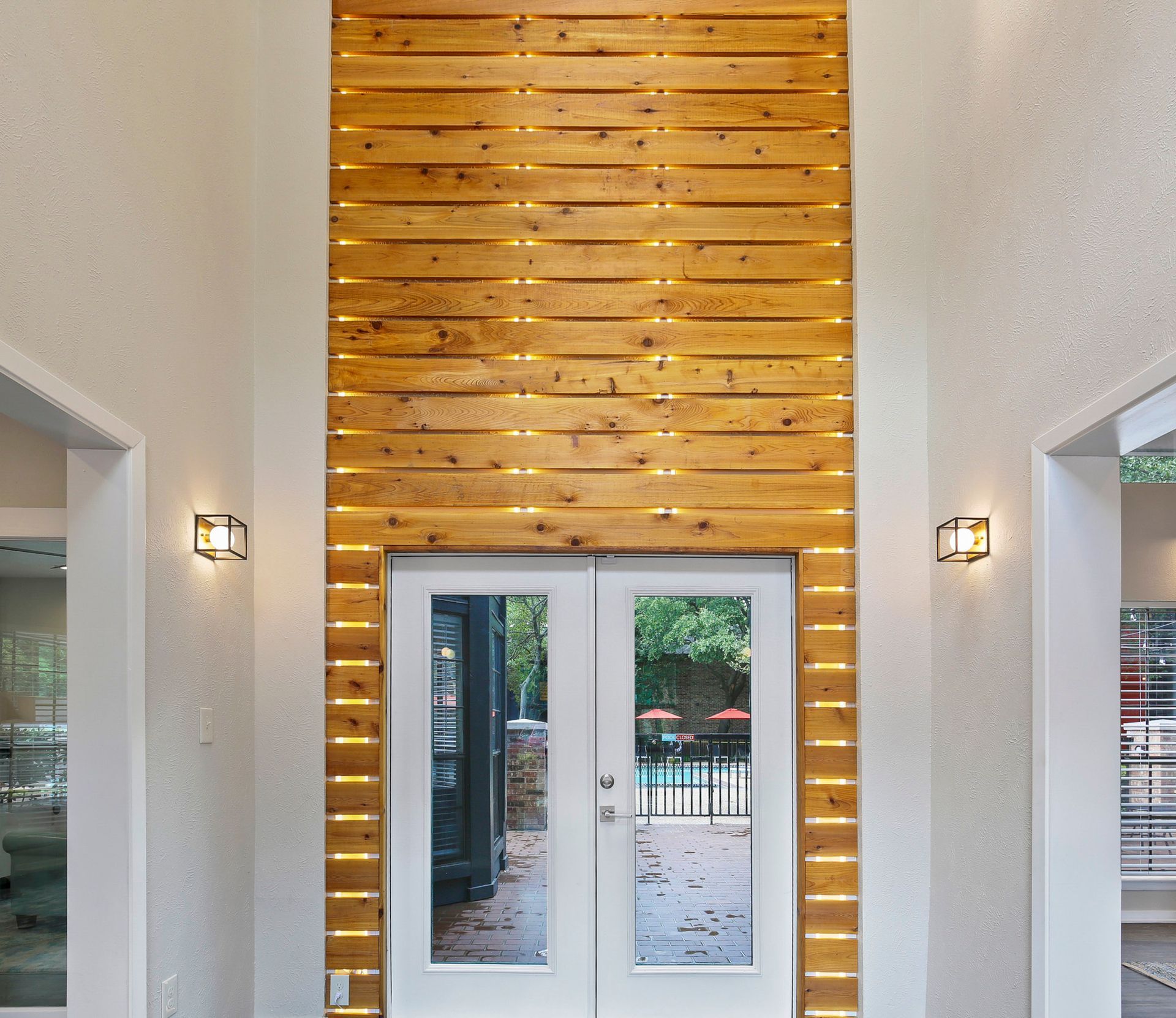 Wooden wall accent above double glass doors, flanked by white walls and sconces.