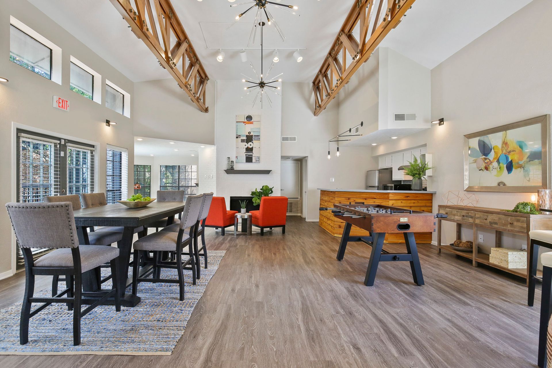 Lounge area with a dark table and chairs, foosball, fireplace, and two orange armchairs.