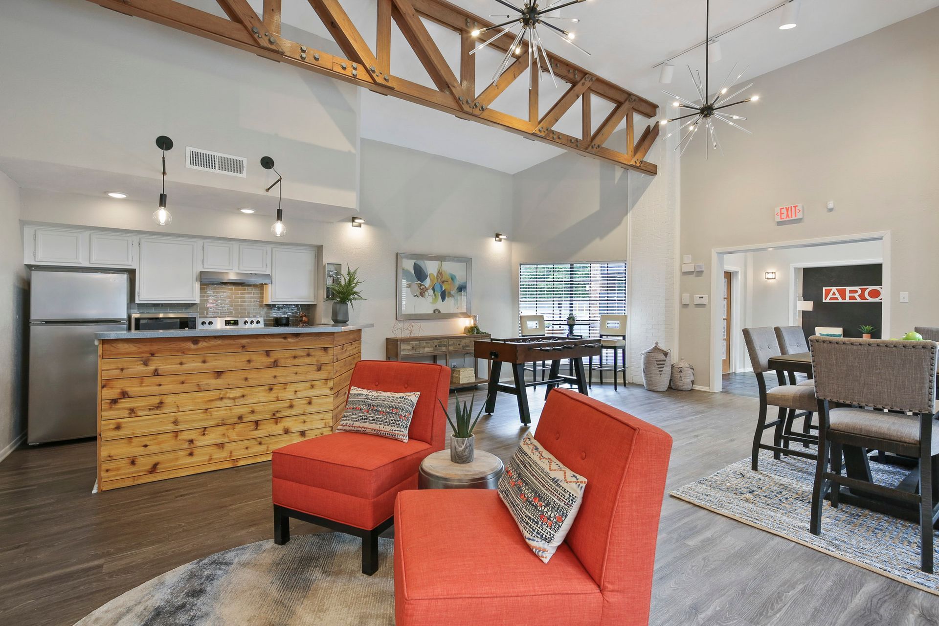 Lounge area with orange chairs, wooden accents, and a kitchen.