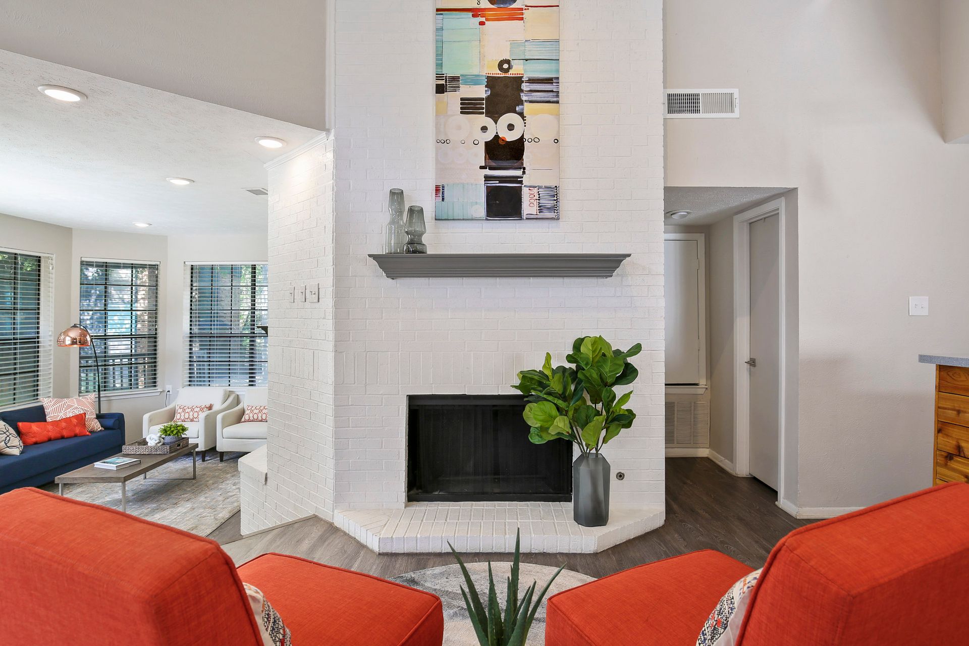 Living room with white brick fireplace, orange chairs, and modern art.