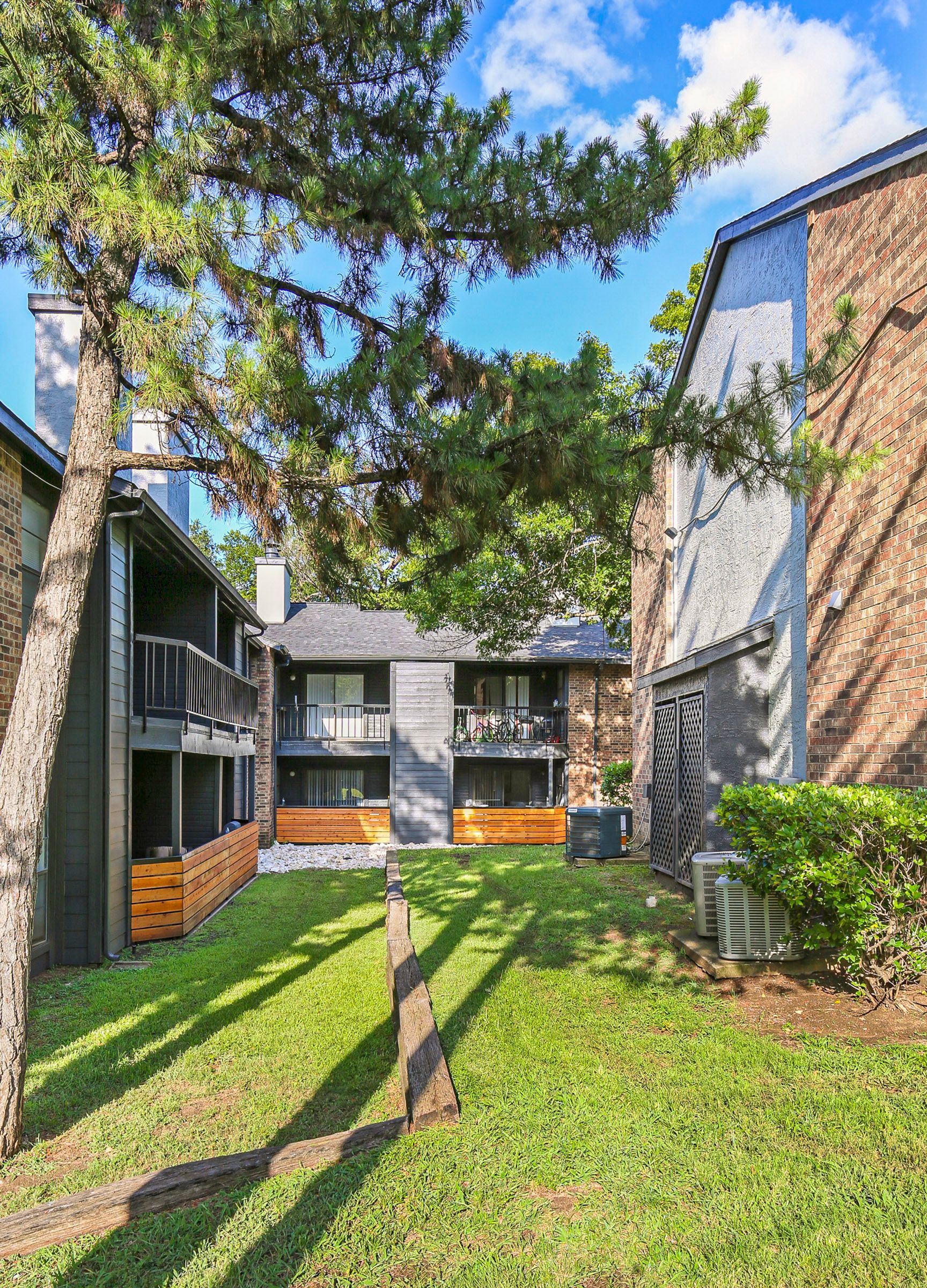 Apartment buildings with balconies, trees, and green grass on a sunny day.