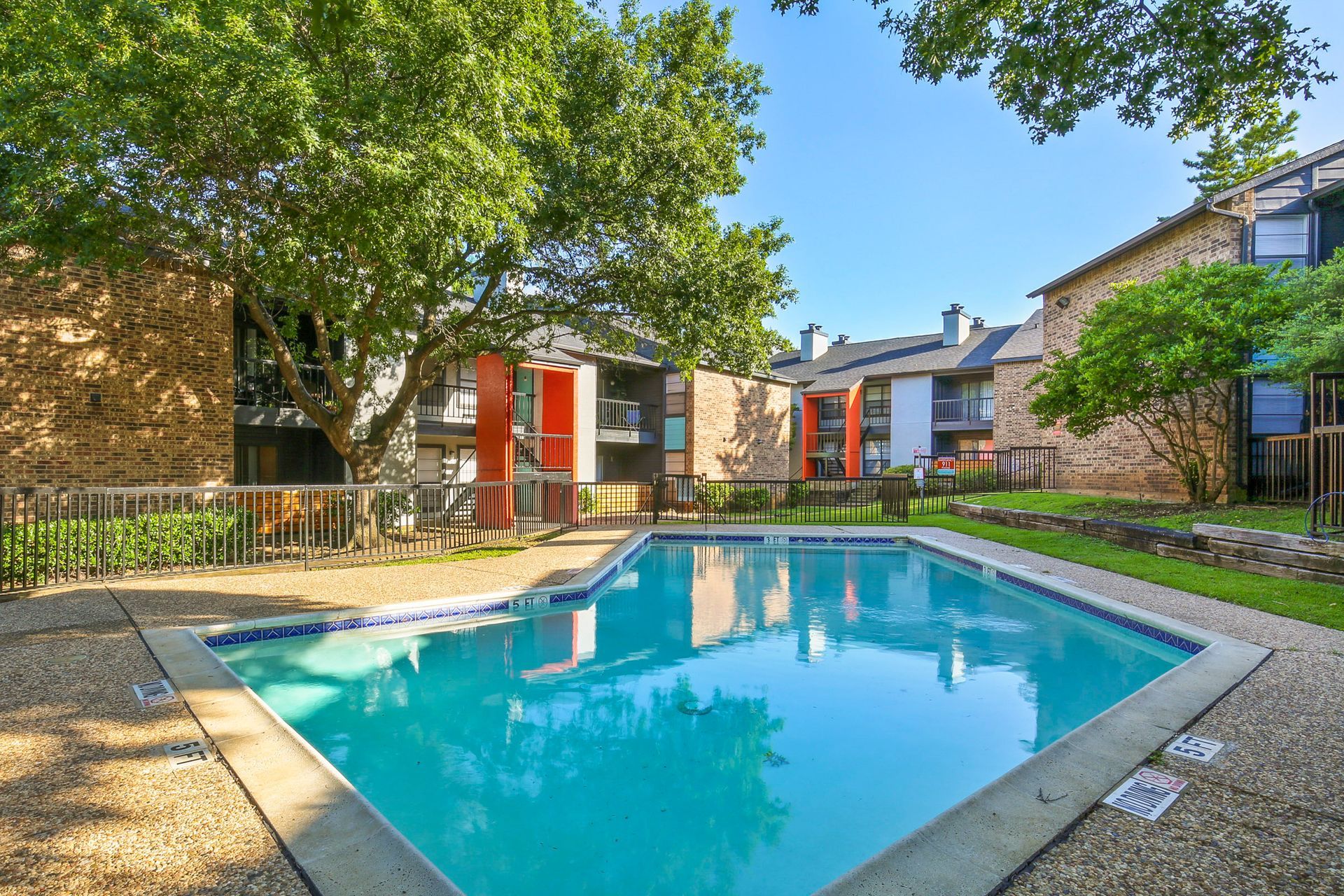 Swimming pool surrounded by apartment buildings with trees on a sunny day.