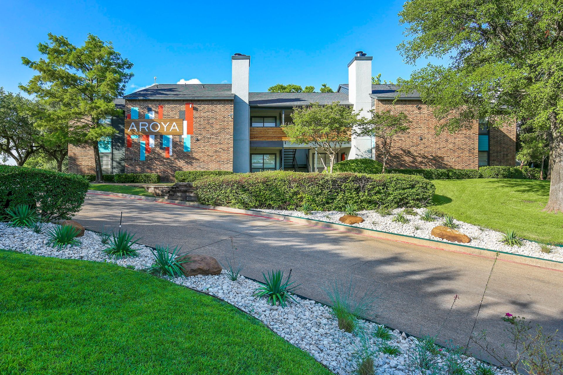 Two-story brick building with a driveway and landscaping, including a colorful mural on the wall.