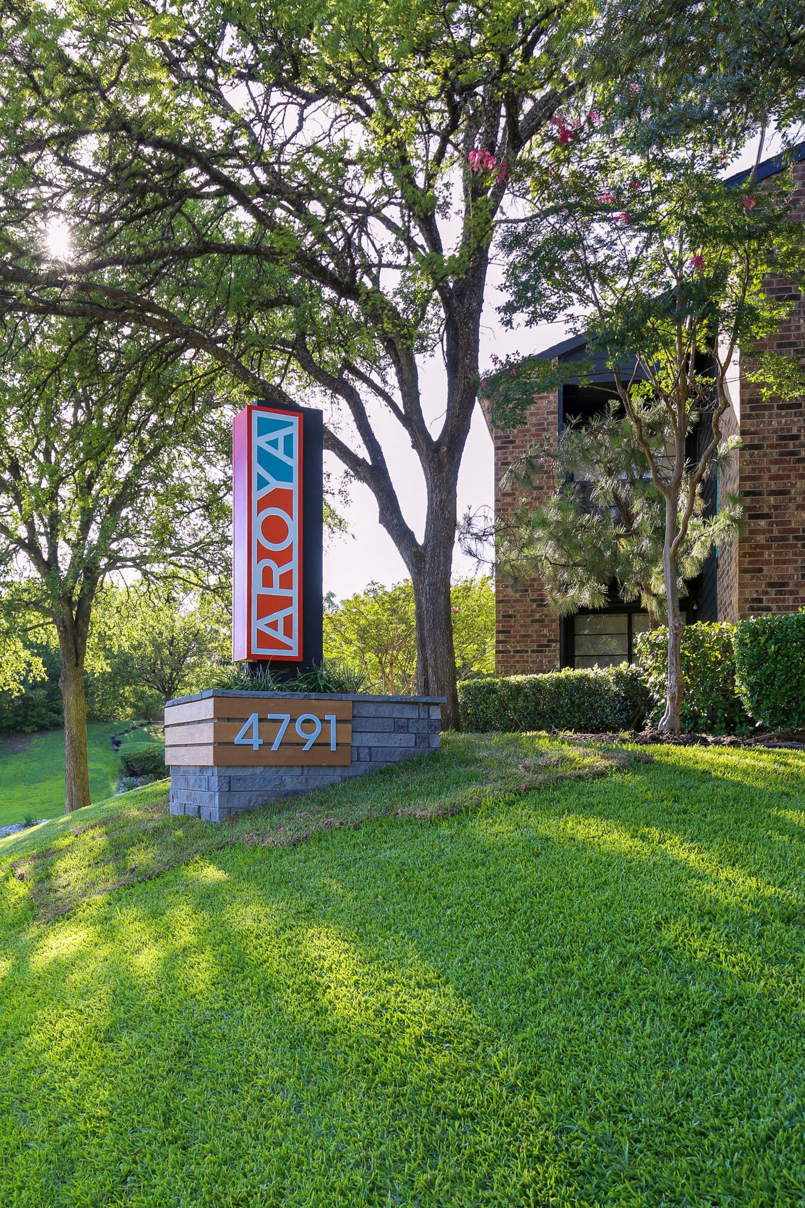 Sign for Aroya apartments, 4791, with colorful logo, in front of a building with greenery.