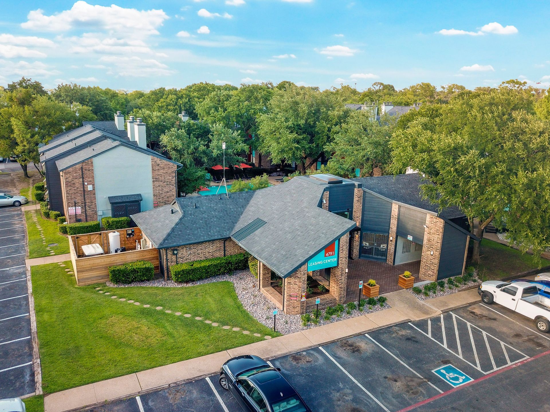 Aerial view of apartment complex with a pool, parking lot, and green space.