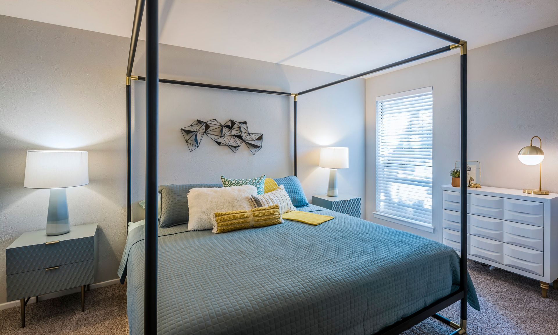 Bedroom with a canopy bed, bedside tables, dresser, and wall art. Soft blue and white color scheme.