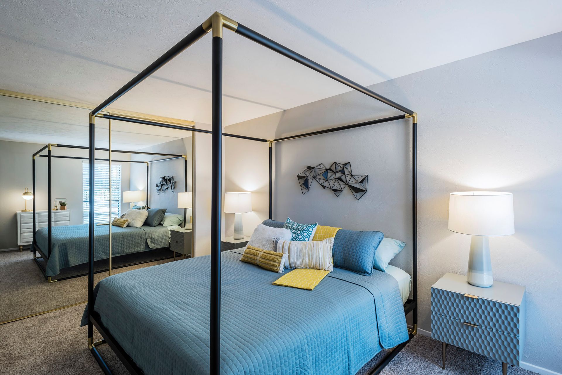 Bedroom with a four-poster bed, mirrored wall, side tables, and decorative pillows.