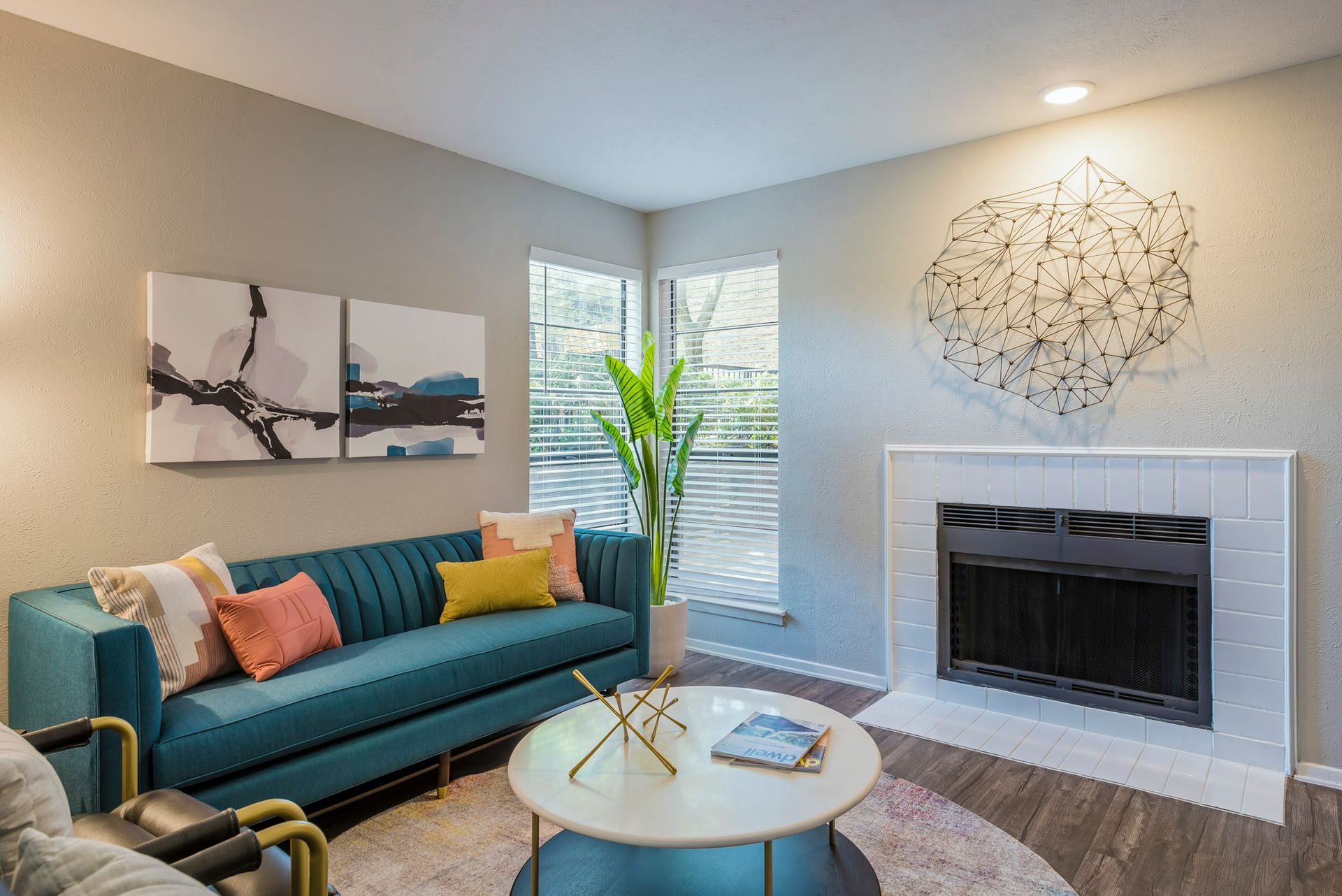 Teal sofa in a modern living room with fireplace, abstract art, and round coffee table.