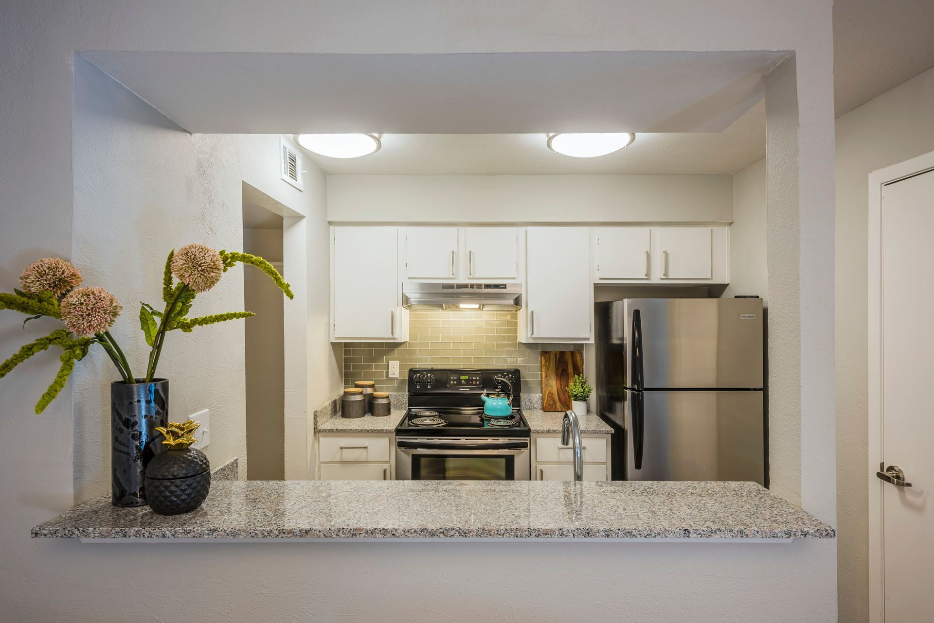 Kitchen with granite countertop bar, white cabinets, stainless steel appliances, and floral arrangement.