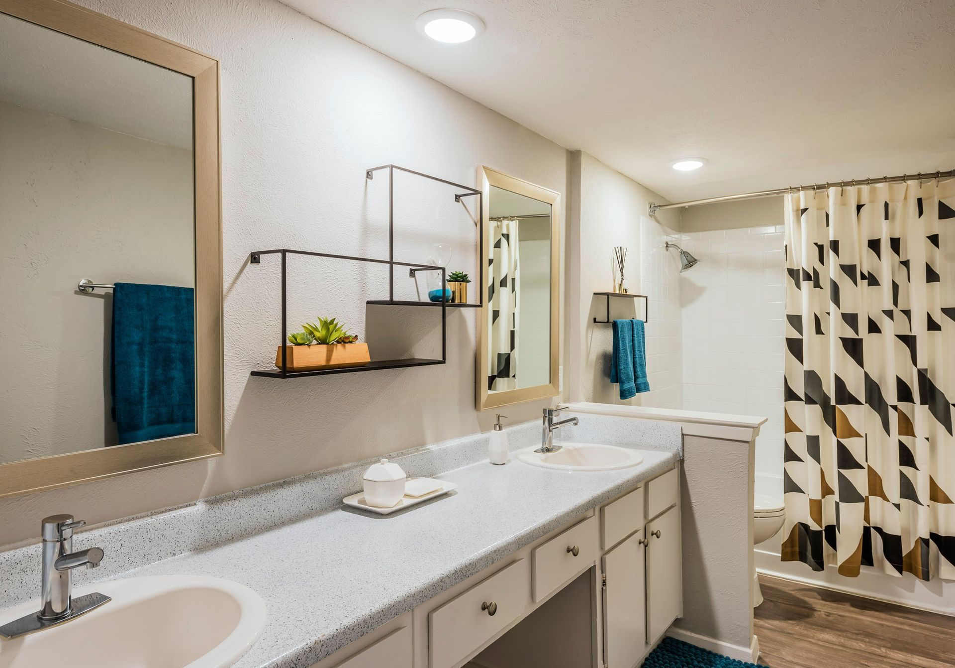 Bathroom with double vanity, mirrors, and shower curtain. Teal towels and decorative shelving.