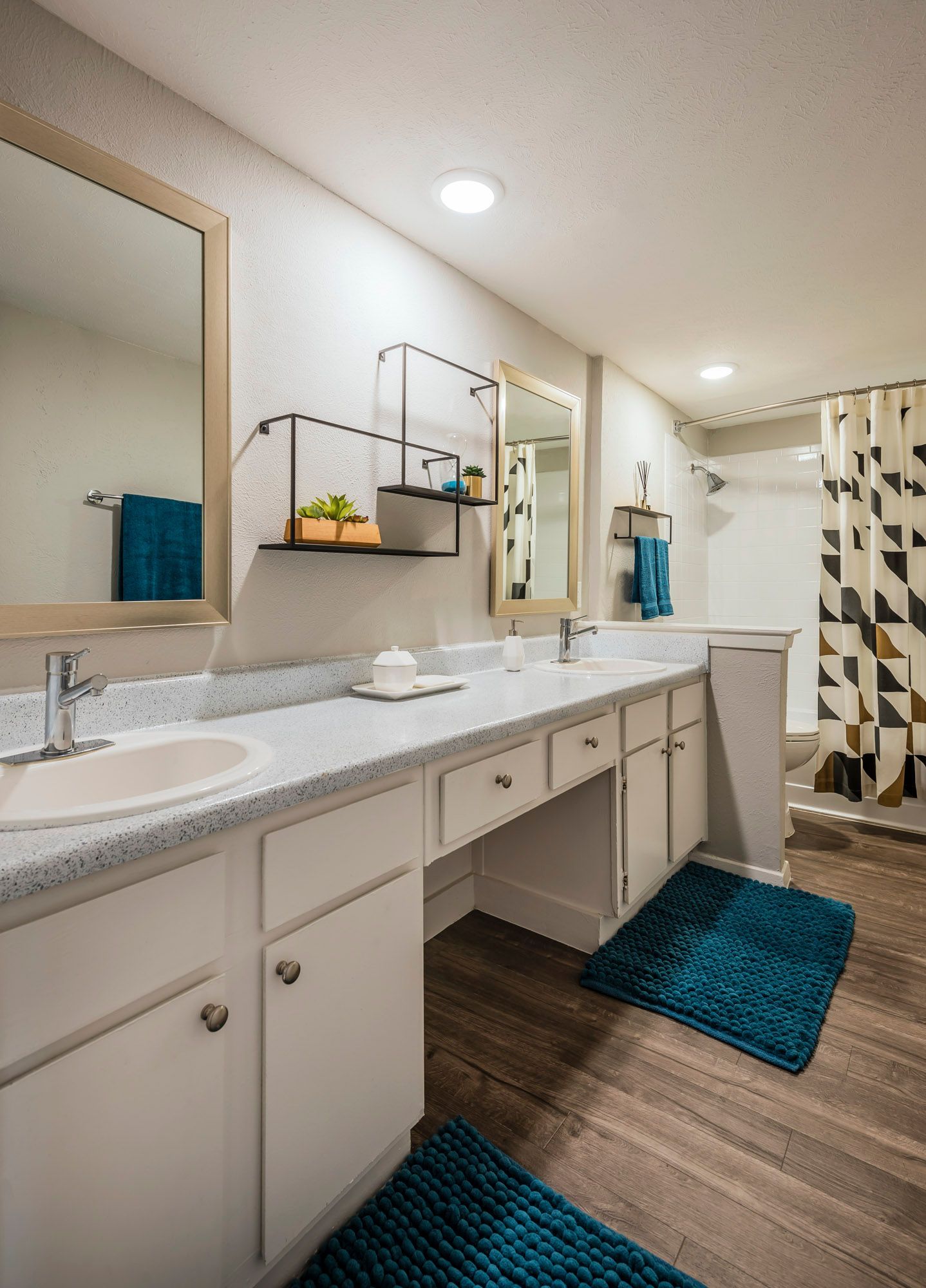 Bathroom with white vanity, sinks, and mirrors. Teal rugs and towels accent the space.