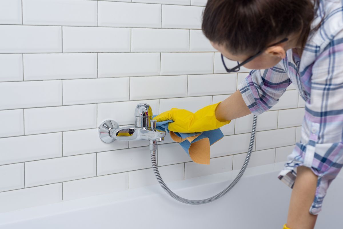 A woman is cleaning a bathtub with a sponge and gloves.