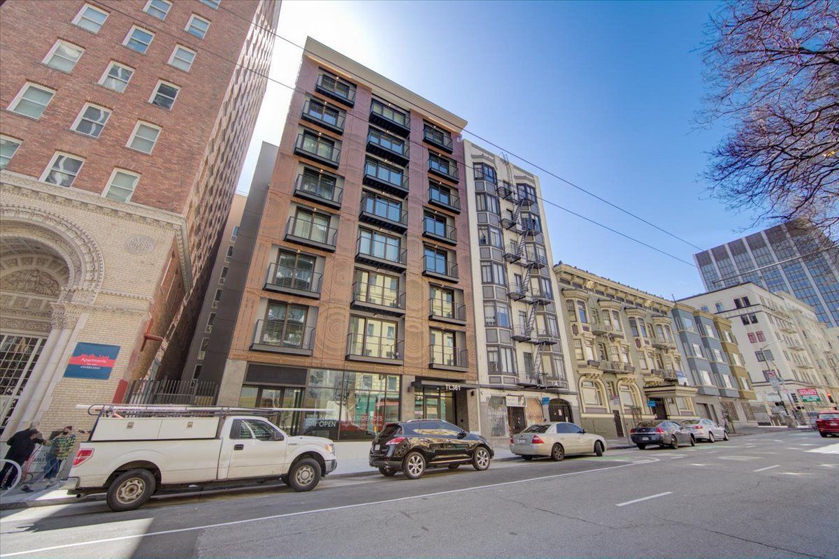 Buildings on a city street with cars parked in front and a clear blue sky.