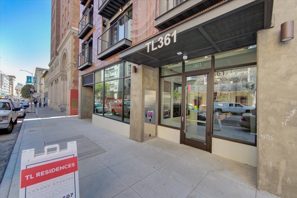 Entrance of a building at 361, with a sign in front; cars and pedestrians on a city street.